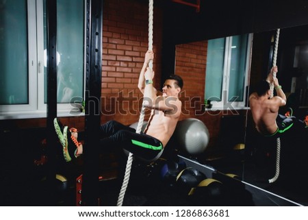Man in training back arms shoulders gets up rope. Black background caucasian brunette.