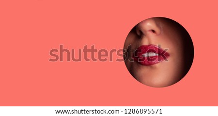 Beauty salon advertising banner with copy space. View of bright lips with glitter through hole in living coral paper background. Make up artist, beauty concept. Cosmetics sale