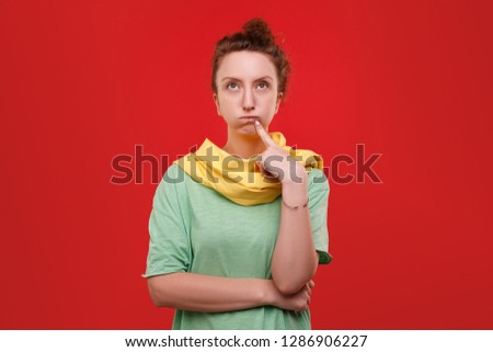 Young cute young woman in a green shirt and yellow scarf posing over a red background. Charming girl makes a list of products for the New Year. Space for advertising.