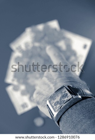 Businessman shows his watch on his wrist and with his hand turned towards the money on the background, monochrome interpretation of the photo.