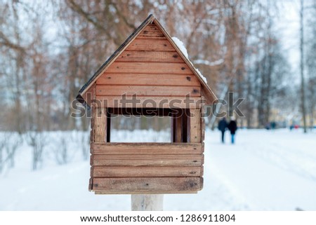 Winter landscape. Wooden birdhouse in snow-covered park. In the distance a couple walking down the path. Blurry photography with a shallow depth of field. Cold winter day.