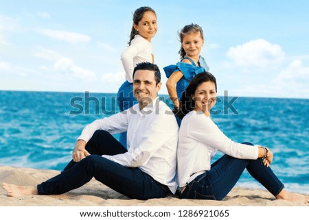 Full length outdoor portrait of attractive young couple with children. Happy family  sitting together on beach looking at camera.