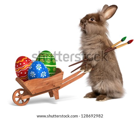Cute Easter bunny rabbit with a little wheelbarrow and some painted Easter eggs, isolated on white, CG+photo