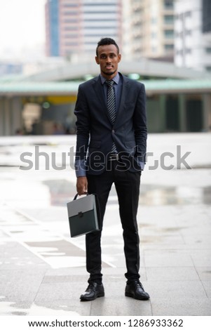 Young African businessman carrying briefcase in the city outdoors