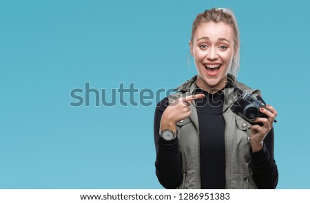Young blonde woman taking pictures using vintage camera over isolated background very happy pointing with hand and finger