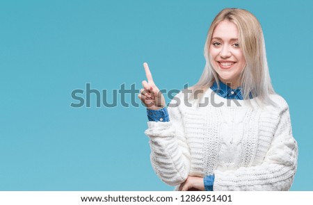 Young blonde woman wearing winter sweater over isolated background with a big smile on face, pointing with hand and finger to the side looking at the camera.