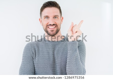 Young handsome man wearing casual sweater over isolated background with a big smile on face, pointing with hand and finger to the side looking at the camera.