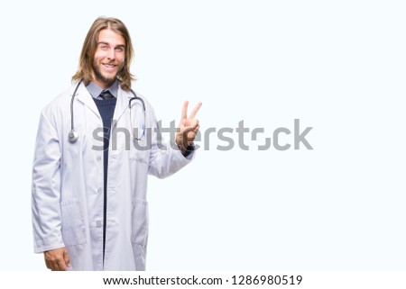 Young handsome doctor man with long hair over isolated background smiling with happy face winking at the camera doing victory sign. Number two.