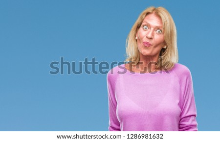 Middle age blonde woman over isolated background making fish face with lips, crazy and comical gesture. Funny expression.