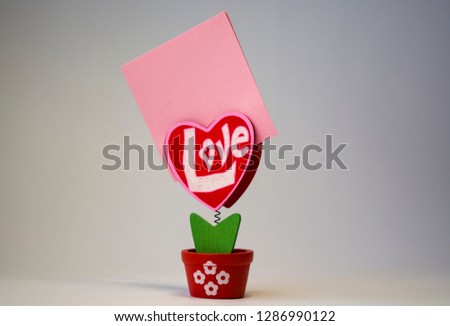 Red wooden heart with the inscription "love". On a spring with a clothespeg in a pot on a white background. Pink sticker.