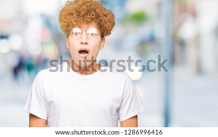 Young handsome man with afro hair wearing glasses afraid and shocked with surprise expression, fear and excited face.