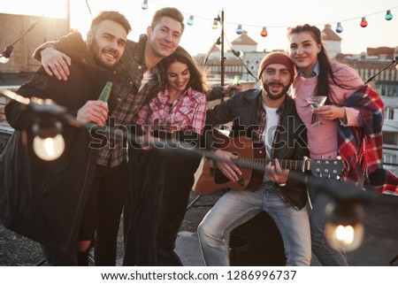 Party at the rooftop. Five good looking friends that posing for the picture with alcohol and guitar.