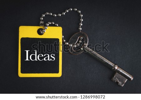 IDEAS inscription written on wooden tag and key on black background with selective focus and crop fragment. Business and education concept