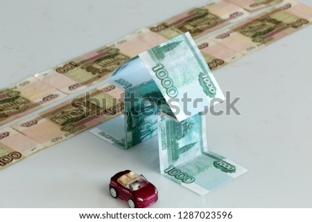 Stylized house of a thousand-ruble notes and toy cars, the road on a highlighted background.
