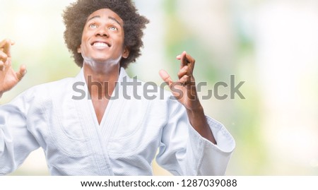 Afro american man wearing karate kimono over isolated background smiling crossing fingers with hope and eyes closed. Luck and superstitious concept.
