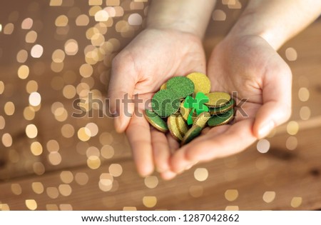 fortune, luck and st patricks day concept - hands holding golden coins and shamrock leaf on wooden background