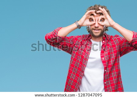 Handsome hispanic model man over isolated background doing ok gesture like binoculars sticking tongue out, eyes looking through fingers. Crazy expression.