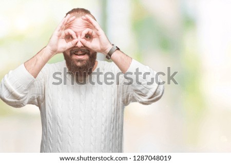 Young caucasian hipster man wearing winter sweater over isolated background doing ok gesture like binoculars sticking tongue out, eyes looking through fingers. Crazy expression.
