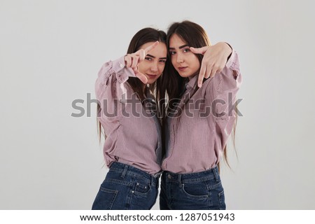 Take the picture of us. Two sisters twins standing and posing in the studio with white background.