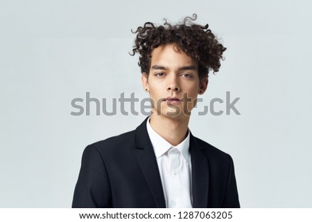Handsome elegant man in a dark suit with curly hair on a gray background