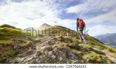A hiker walking up a mountain ridge, The Edge, towards Ullock Pike, Carl Side and Skiddaw in the English Lake District UK. Royalty-Free Stock Photo #1287066661