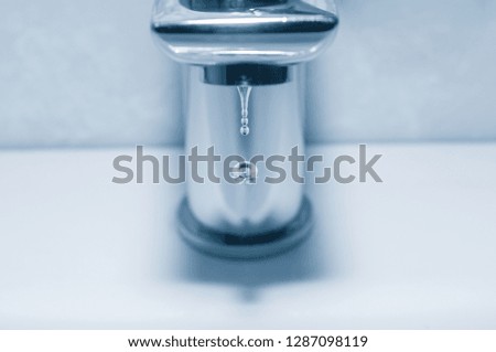 Faucet and falling drops close up on blue background