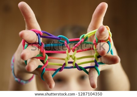 Child playing classic, old-school string game and didactic toy with her fingers, shaping butterfly, developing her motor skills. IQ, education, intelligence, fun and childhood concept.  Royalty-Free Stock Photo #1287104350