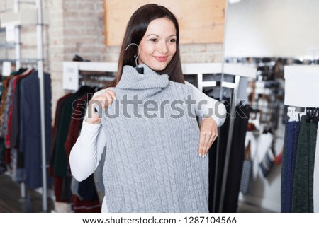 Portrait of smiling woman choosing sweater in the modern shop