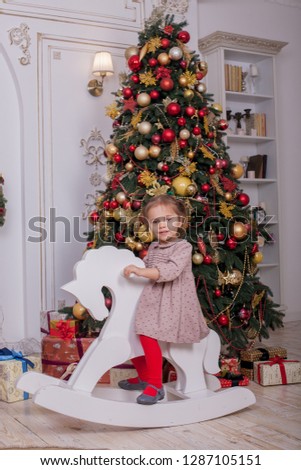 Little beautiful girl child riding a wooden toy horse under the Christmas tree with gifts