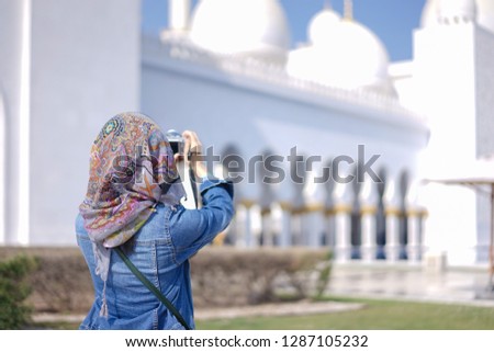 Tourist at grand mosque. An unidentified female tourist is taking a photo of the Sheikh Zayed Grand Mosque, Abu Dhabi, UAE. With selective focus on the colorful turban.