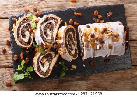 Festive glazed poppy beigli cake with raisins, walnuts close-up on a wooden table. horizontal top view from above
