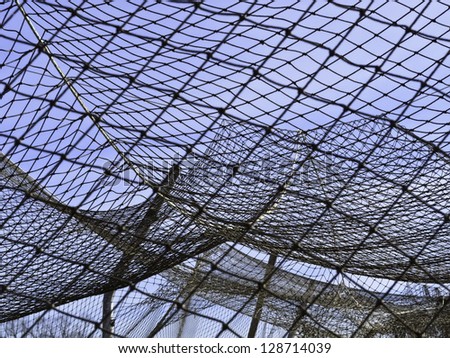 Complexities of practice: Part of netting over batting cage by baseball field on campus of community college Royalty-Free Stock Photo #128714039
