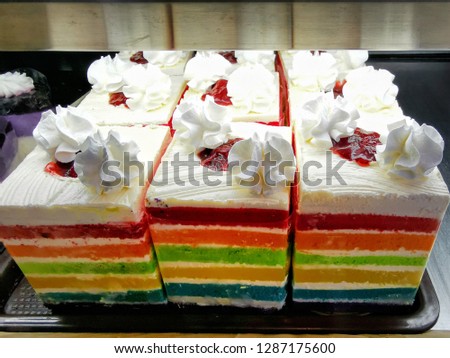 Rainbow layer cake on the white tray in glass cabinet​ at​ coffee​ shop.