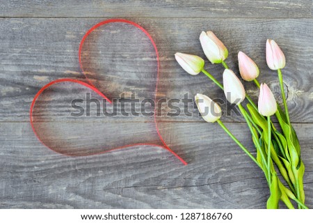 Tulips with pink tint with ribbon in the form of a heart of the color of living coral on a wooden vintage background. Romantic card concept.