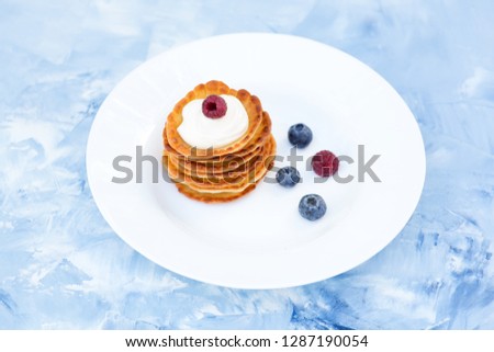 A stack of delicious pancakes with sour cream, raspberries and blueberries on a light background. with copy space
