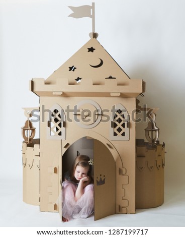 Sad beautiful little girl in princess dress playing with her toy castle.