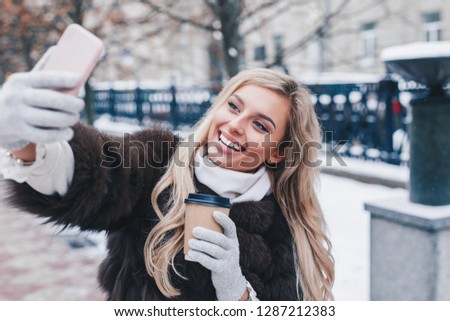 Beautiful girl takes funny winter selfie on city street
