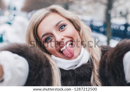 Beautiful girl takes funny winter selfie on city street