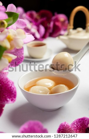Chinese New Year concept picture. A bowl of dumpling with black sesame and ginger. Tea pot and a glass of tea in the background.