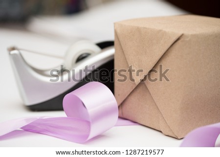 Wrapping a package in brown paper. Tying a gift or present in lavender or purple satin ribbon. Tape, gift, package, ribbon, bows.
