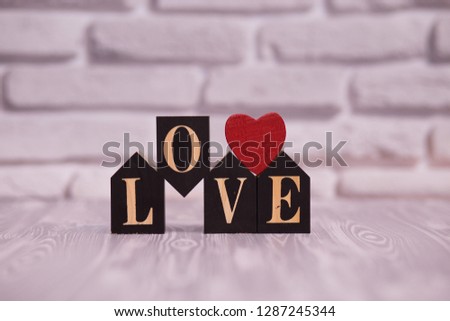 Text love on black wooden blocks with red heart on white brick background.