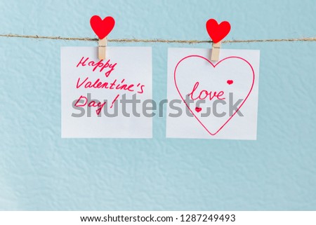 Red Valentine's love hearts pin hanging on natural cord against blue background. drawn heart on paper piece.