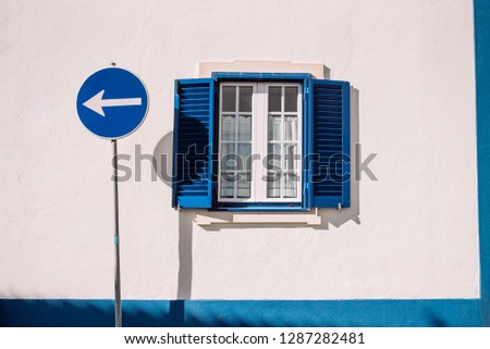 Blue arrow traffic sign turn left in the town. Road signs in the journey. Window with blue shutters.