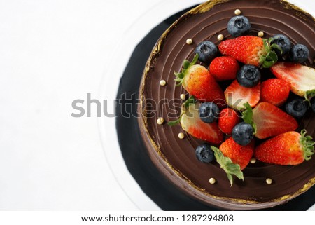 Fresh delicious chocolate cake with blueberries and Strawberries on stand and against white background. Copyspace for text - Image        