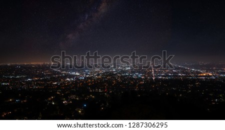 Beautiful super wide-angle night aerial view of Los Angeles, California, USA, with downtown district and mountains with sky full of stars and milky way, seen from the Griffith Park observatory.