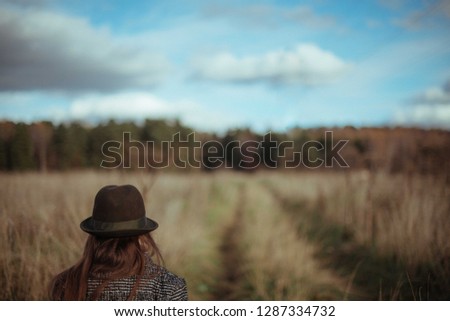 A young woman is walking along a country road on a sunny day in autumn. A girl in a coat and hat walks along a deserted road in a village in the field