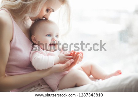 Young pretty mother with her little baby at home. Mom and daughter indoors.  month child with her parent in the bedroom.
