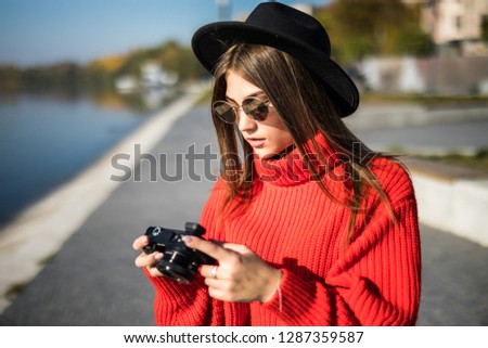 Happy stylish woman hipster holding photo camera and smiling at sunny shore near water on pier
