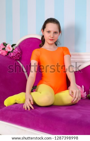 beautiful girl model in children's colored gymnastic Leotard and colored tights posing in a Photo Studio and smiles about fine sofa and throws up long hair up