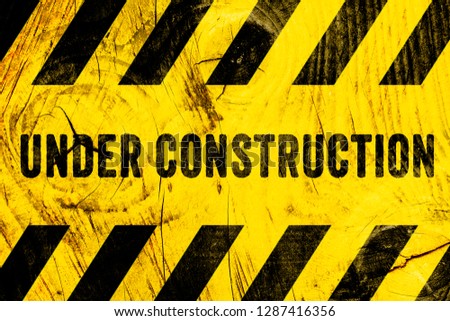 Under construction warning sign text with yellow black stripes painted on wood wall plank texture wide background. Concept under construction do not enter the area, caution, danger, construction site